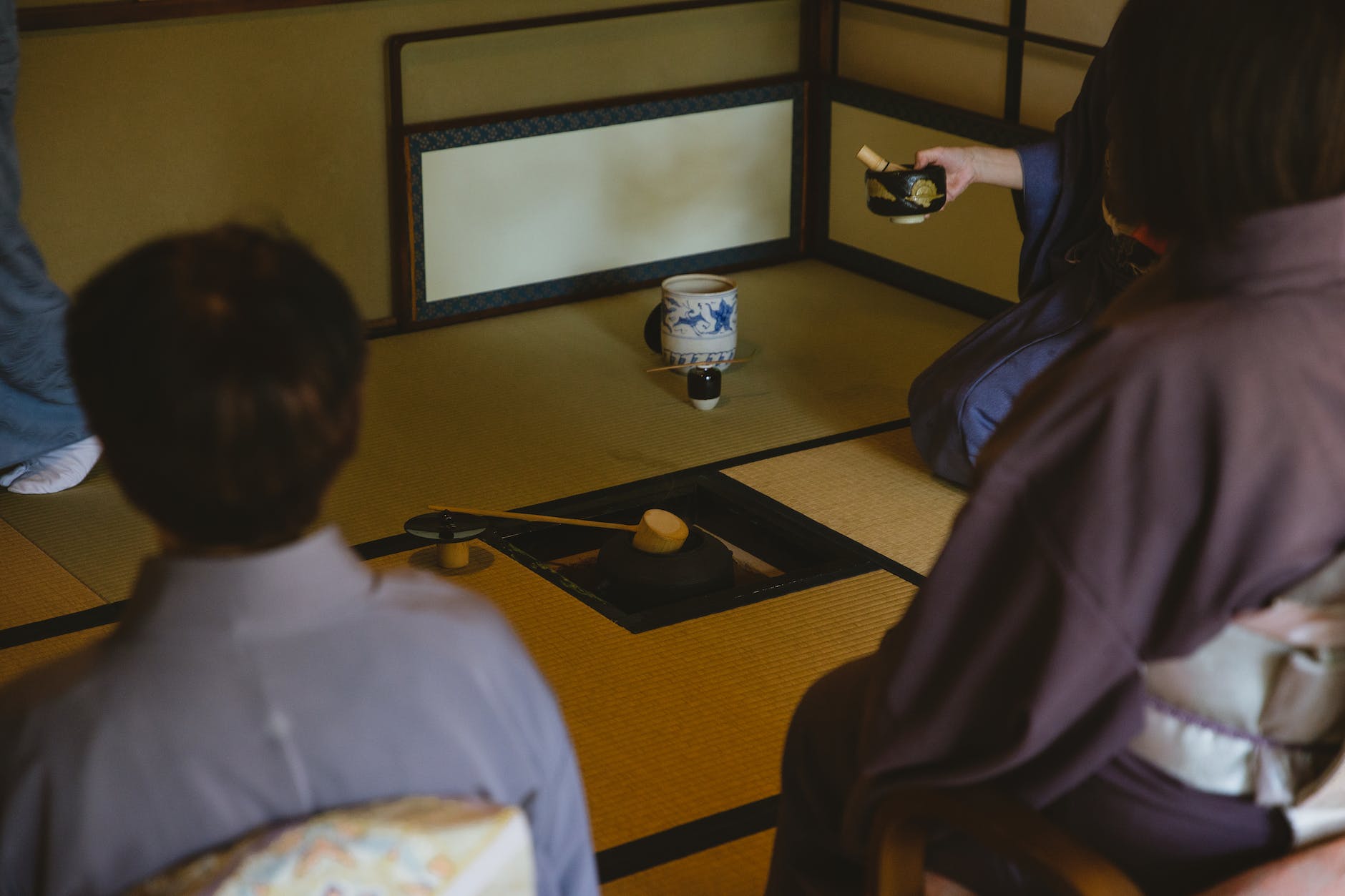 unrecognizable people in kimonos sitting on tatami in tea room