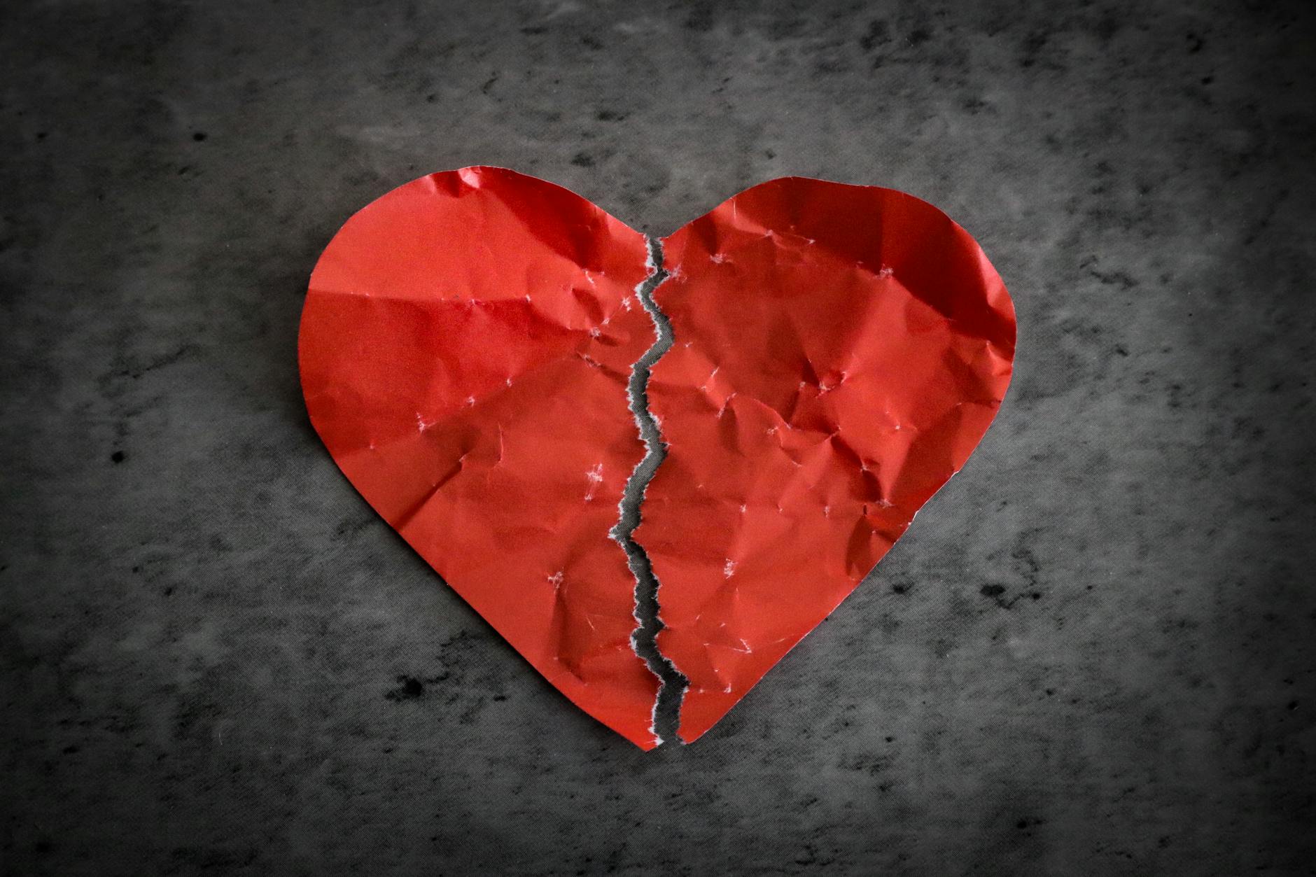 red paper heart ripped in half on dark background broken heart separation concept