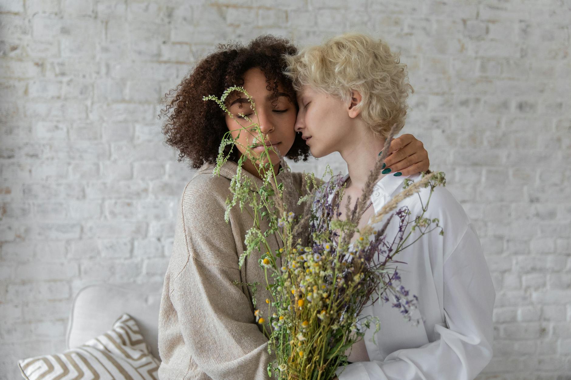 tender multiethnic women with wildflowers embracing in room