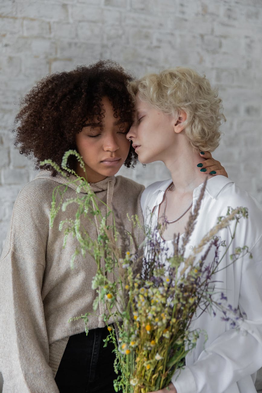 peaceful multiracial women with flowers hugging in room